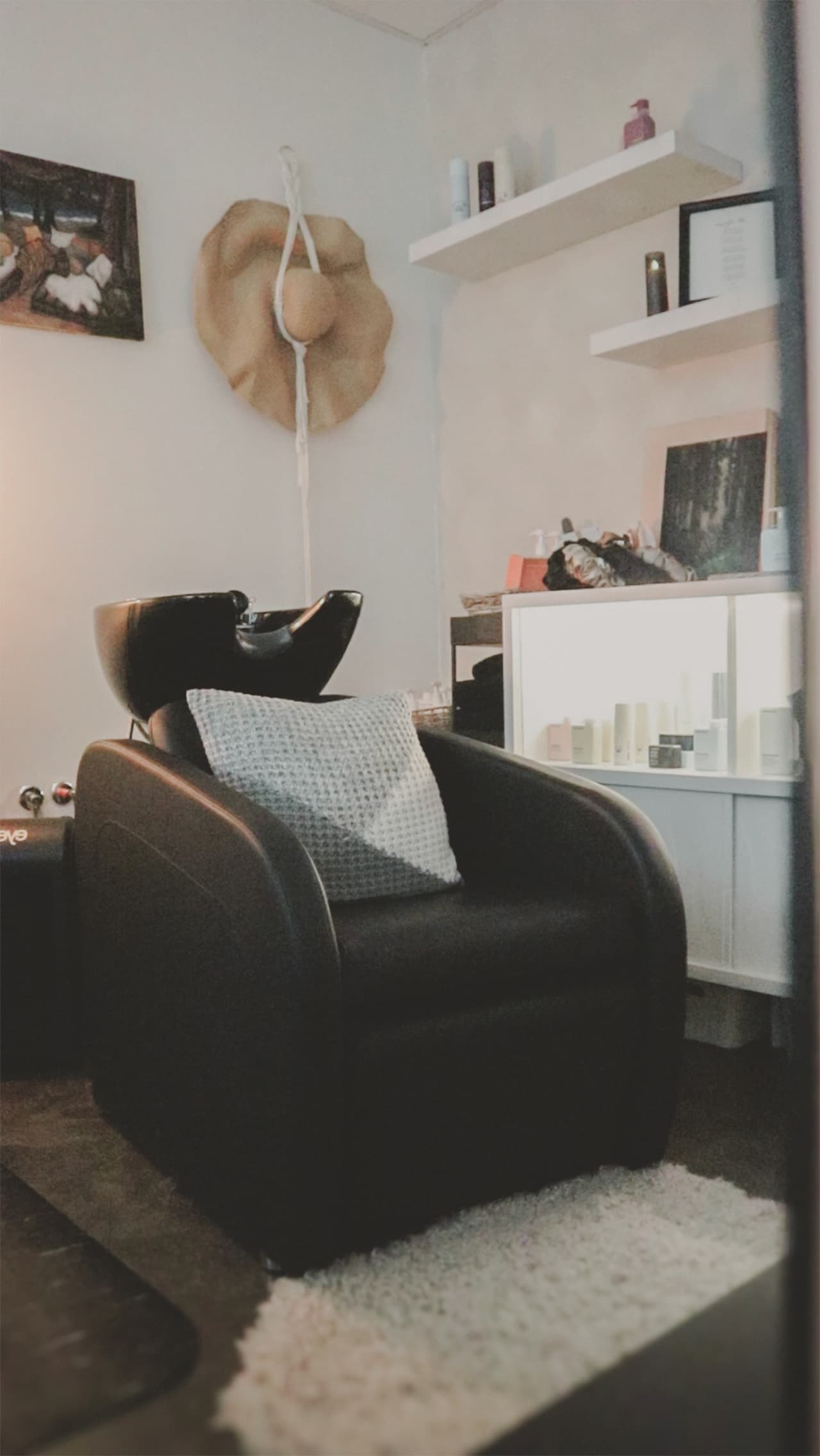 The Sanctuary's wash station: a black shampoo chair and basin on a white rug, with floating shelves and lit product shelves beside it